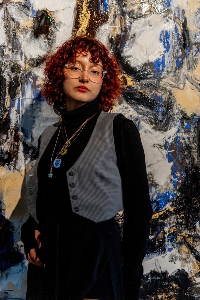 Stylish woman with curly hair posing in front of a vibrant abstract painting.